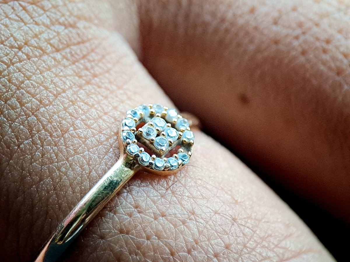 Gold ring with clear gemstones in a halo setting worn on a finger